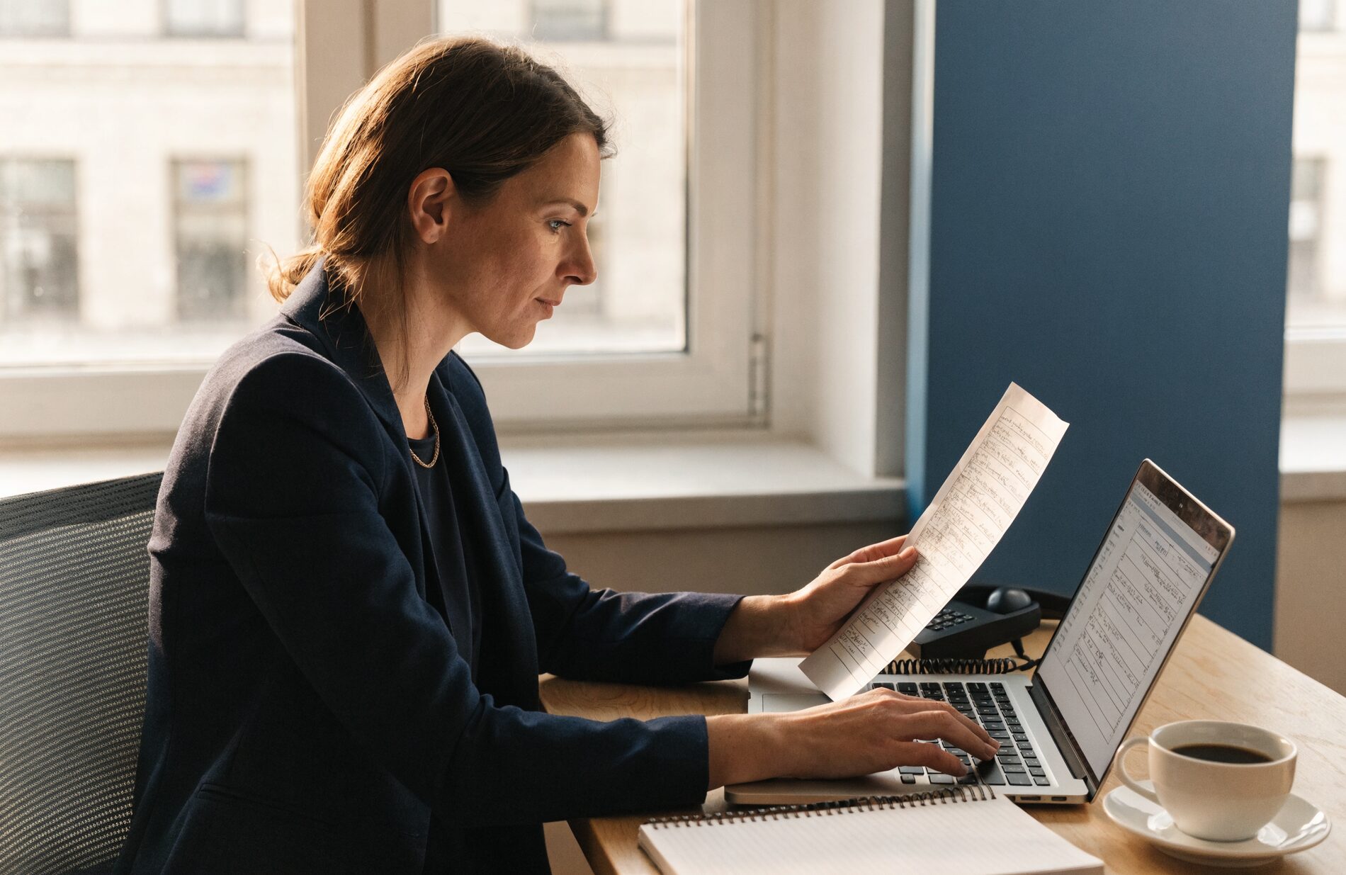 A compliance lead reviewing a printed call and consent log beside her laptop and desk phone